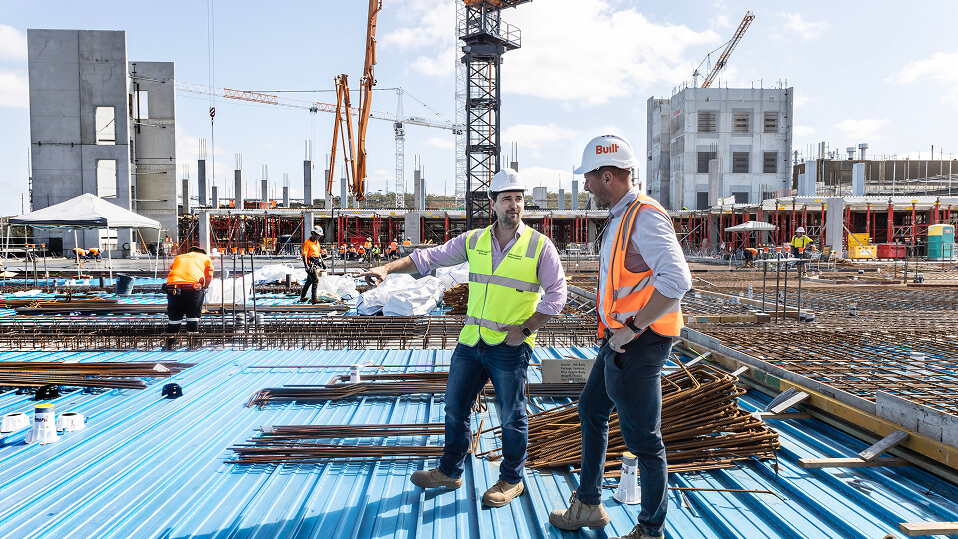 Two project staff stand among steel reinforcement and formwork while discussing progress on the QEII Hospital expansion.