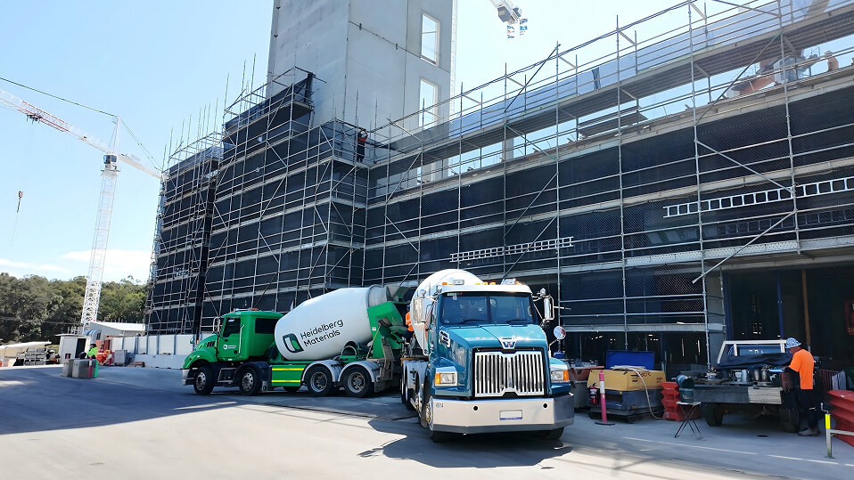 Concrete trucks and workers operate beside a scaffolded building during construction of the QEII Hospital expansion.