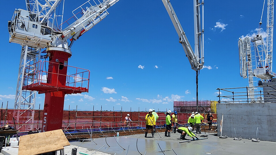 Construction workers pour and level concrete on an upper floor of the Logan Hospital expansion using large cranes and pumping equipment.