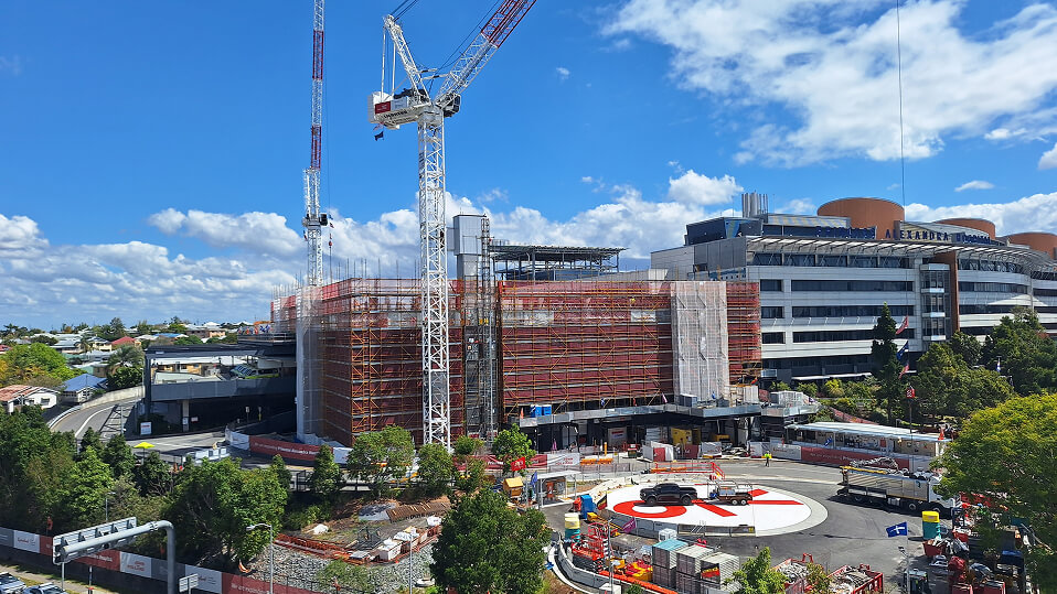Construction cranes and scaffolding surround the Princess Alexandra Hospital expansion beside the active helipad.