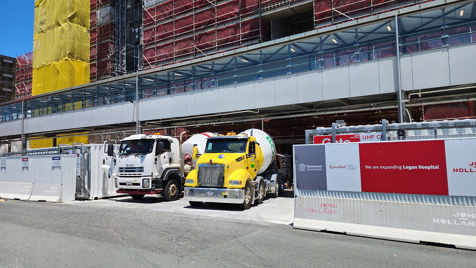 Concrete trucks and construction fencing line the site of the Logan Hospital expansion beside the scaffolded building.