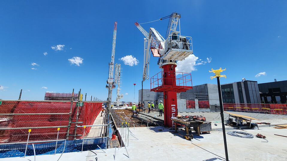 Workers and cranes operate on the top level of the Logan Hospital expansion amid scaffolding and safety barriers.