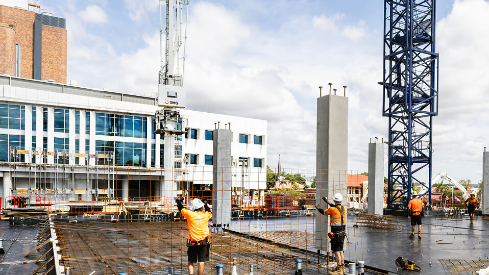 Construction workers install steel reinforcement and concrete columns as cranes operate around the Ipswich Hospital expansion site.